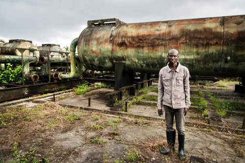 Image shows person stood infront of oil tanks in the Niger Delta