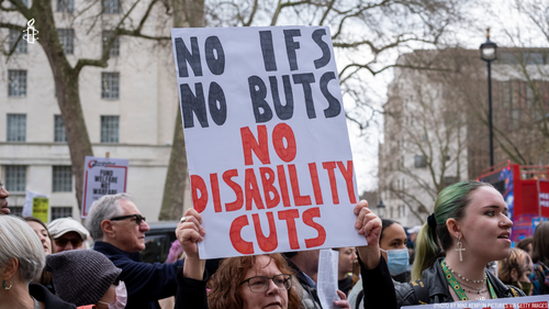 Woman holding placard that no ifs no buts no disability cuts