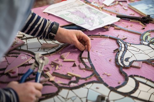 The artist's hand places ceramic pieces in a mural