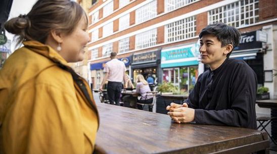 Two people talking at a table outside