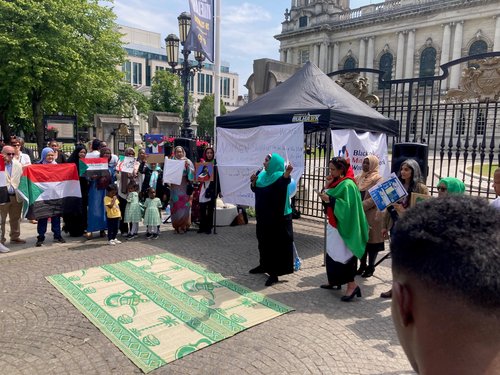 Vigil for peace, justice and accountability for war crimes in Sudan - Belfast, June 2023. Image shows speaker and supporters, many holding Sudan flags, in front of Belfast City Hall