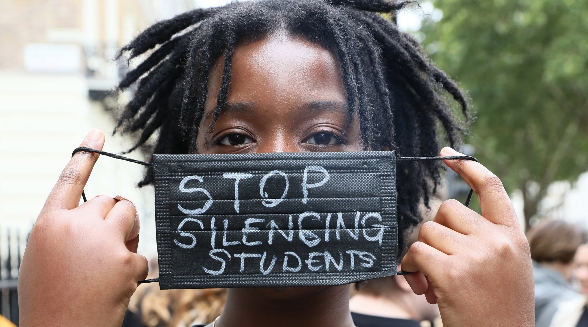 Image shows student holding mask in front of their face with the words "Stop silencing student"