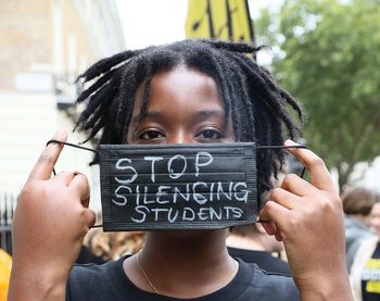 Image shows student holding mask in front of their face with the words "Stop silencing student"