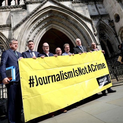 Journalists stood in from the Royal Courts of Justice holding a banner reading journalism is not a crime