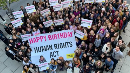 A group of few dozen people holding a banner saying Happy Birthday Human Rights Act