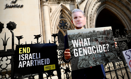 Photo featuring a masked figure of Keir Starmer holding a placard denying the mass atrocities in Gaza