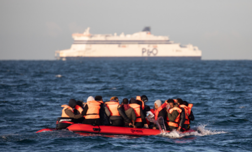 Migrants packed tightly onto a small inflatable boat bail water out as they attempt to cross the English Channel near the Dover Strait