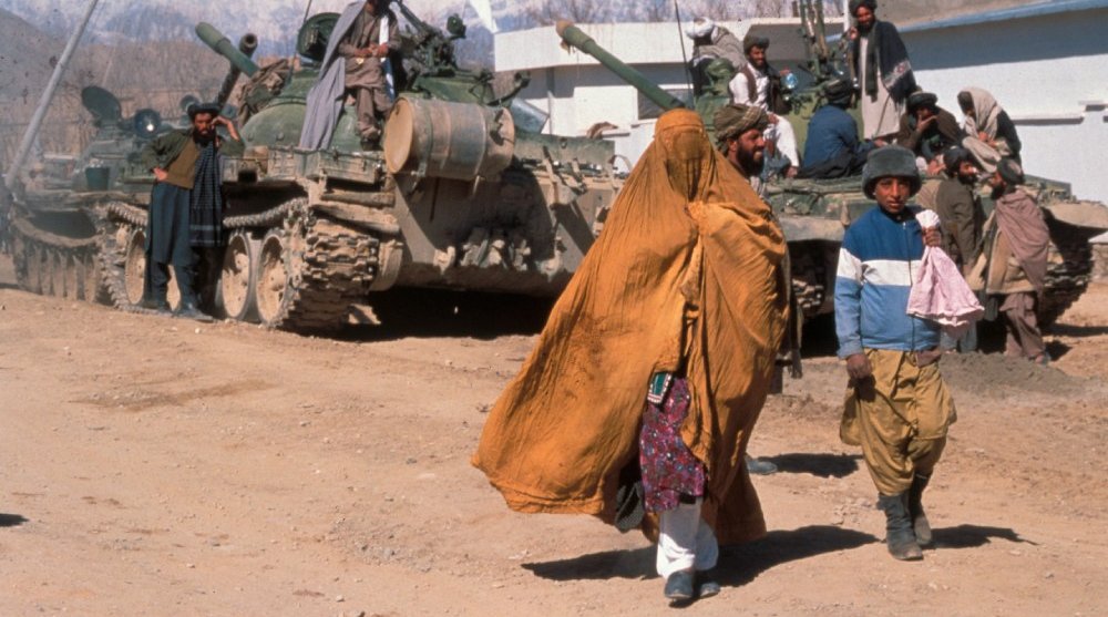 Afghan woman and boy walk by a tank in Kabul, 2004