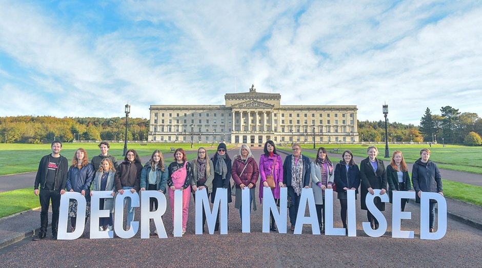 A row of campaigners holding large letters that spell 'DECRIMINALISED' stand outside the Stormont building in Northern Ireland