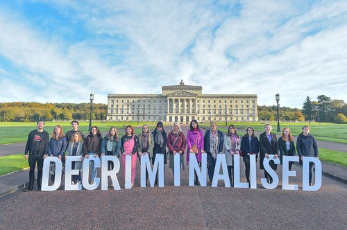 A row of campaigners holding large letters that spell 'DECRIMINALISED' stand outside the Stormont building in Northern Ireland