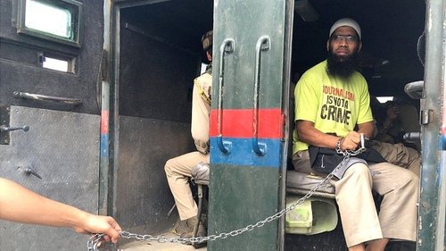 Picture of a man being held in chains in a military vehicle.