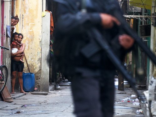Residents look on as military police officers patrol in Complexo da Mare, favela