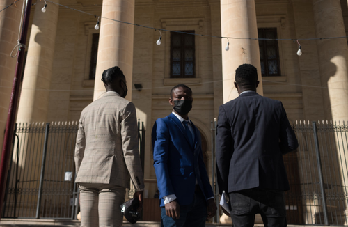 The El Hiblu three stand outside old building wearing suits on three-year anniversary of their rescue at sea