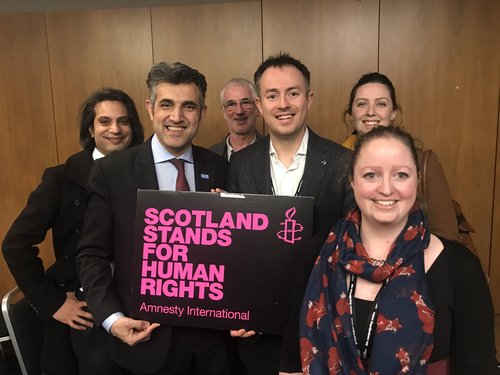 A group of people hold up an Amnesty International placard that says 'Scotland stands for human rights'
