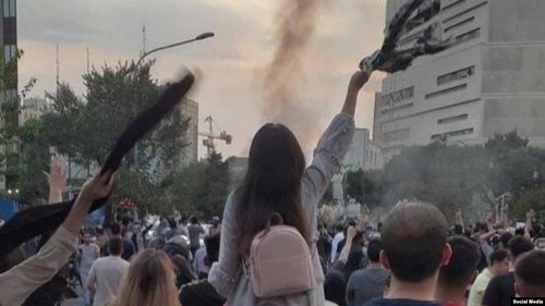 A person sits on someone's shoulders at a protest and waves a scarf