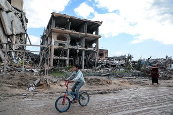 A photograph of a young boy cycling through the decimated Gazan landscape