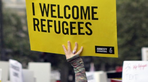 Person holding 'I Welcome Refugees' placard